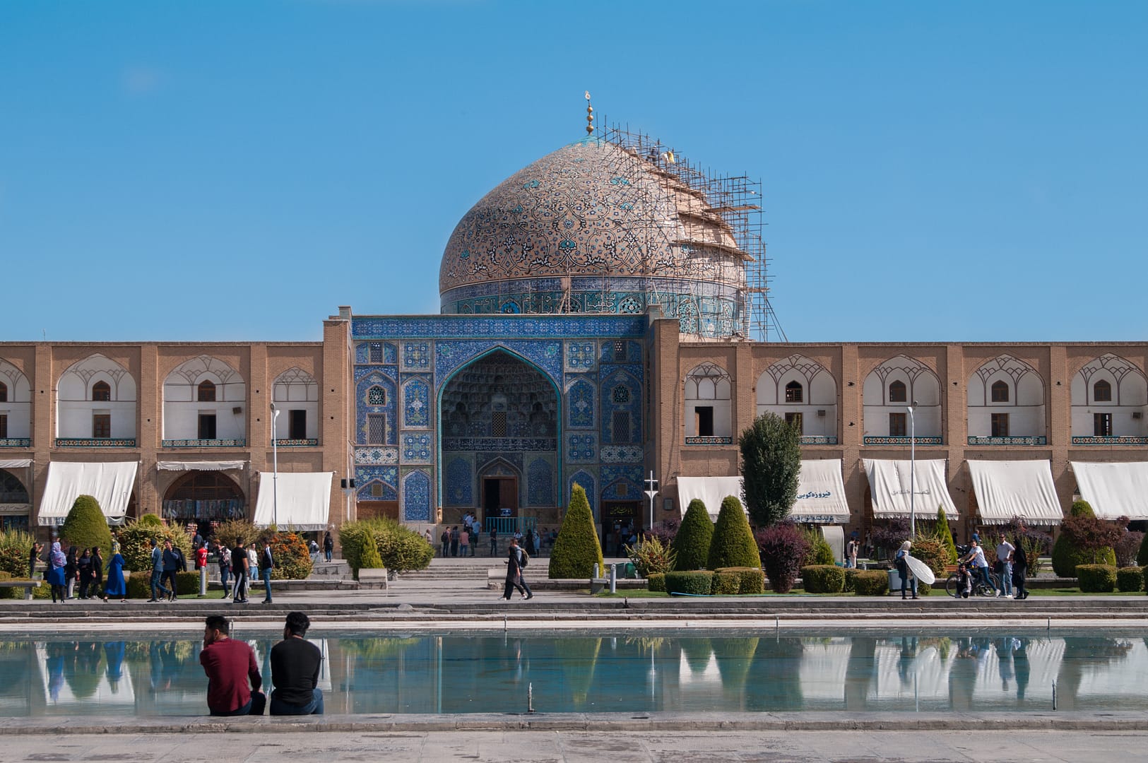 Deux hommes sont assis devant un bassin d'eau qui fait face à la mosquée Loutfallah à Ispahan
