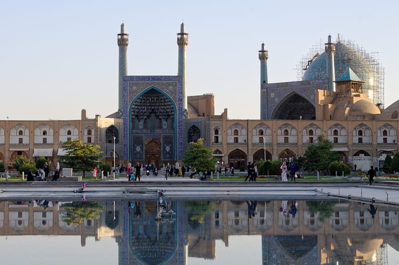 La mosquée de l'Immam prise de face au coucher du soleil avec un bassin d'eau au premier plan